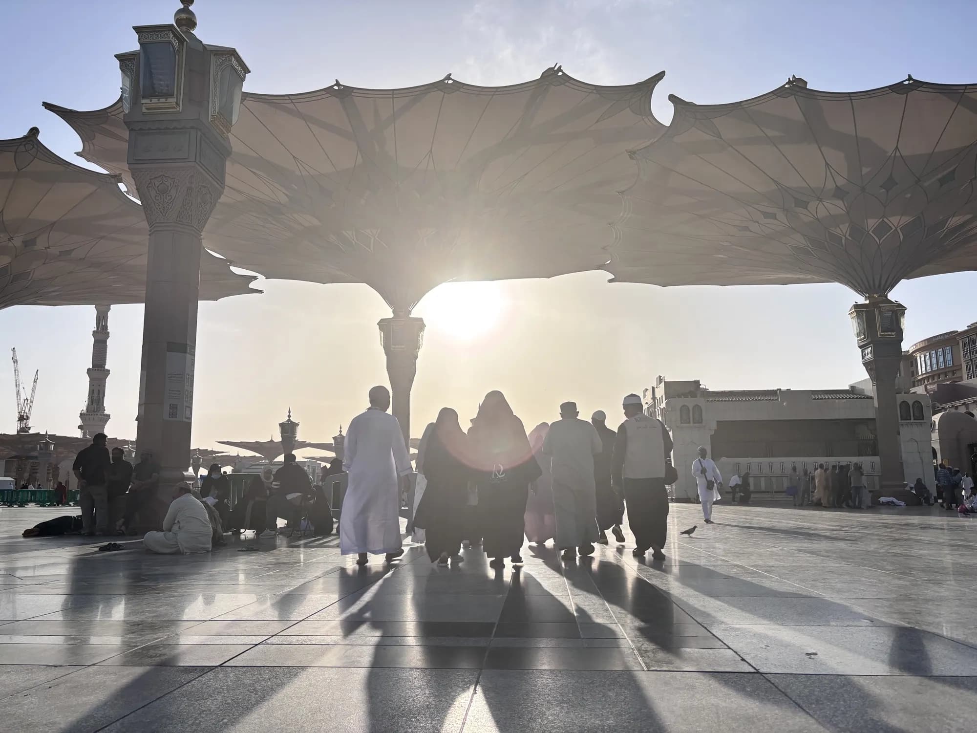 Jamaah umroh K2 berjalan di pelataran Masjid Nabawi dengan payung raksasa saat senja